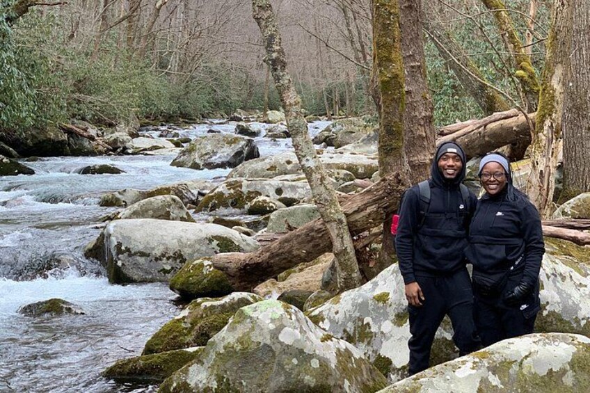 Dos personas de pie junto a un río con rocas y árboles. 2