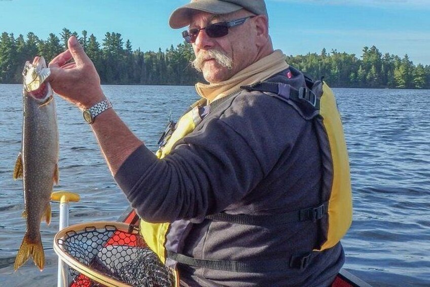 En person holder en fisk om bord på en båd med en sø og træer i baggrunden. 2