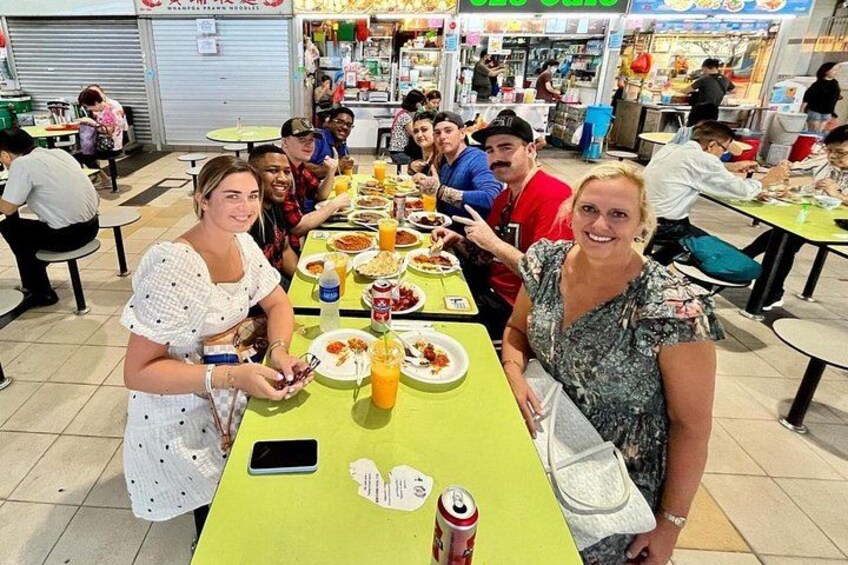 Een groep mensen dineert in een restaurant met tafels, stoelen en verschillende gerechten. 1