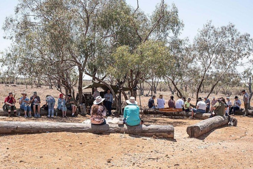 A group of people sitting under trees in a dry, open landscape. 5
