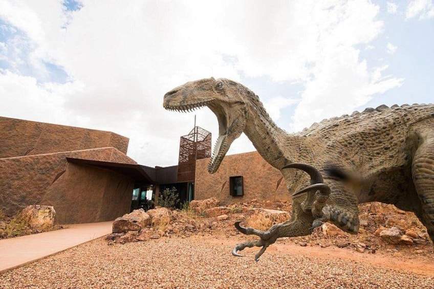 Una gran escultura de dinosaurio en un paisaje desértico con un edificio moderno al fondo. 1