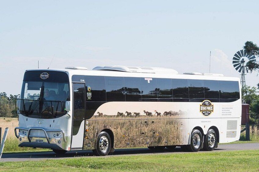 Un autobús grande de color blanco con superficie reflectante, estacionado en una carretera con un molino de viento al fondo. 2