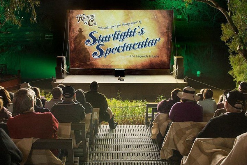 An outdoor movie screening with an audience seated on tiered benches. 2