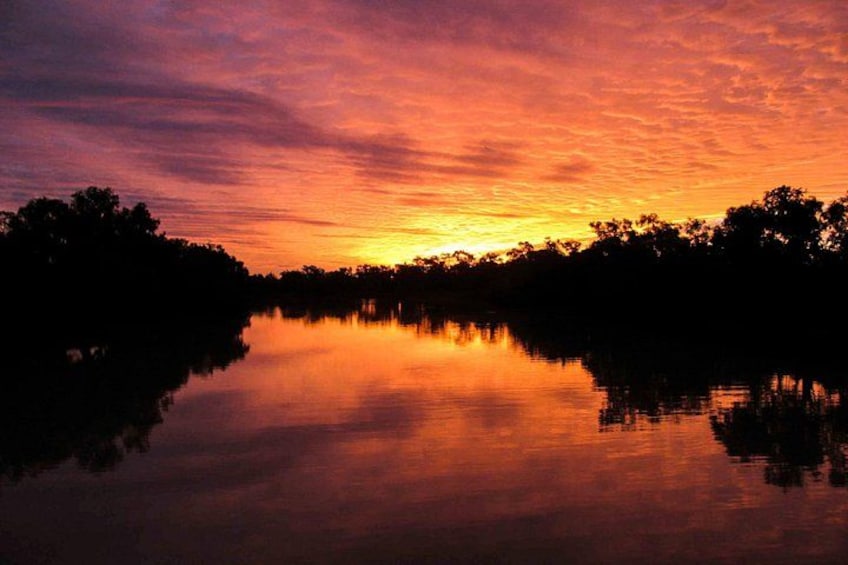 Een zonsondergang boven een rustige rivier, met bomen als silhouetten tegen de lucht. 2