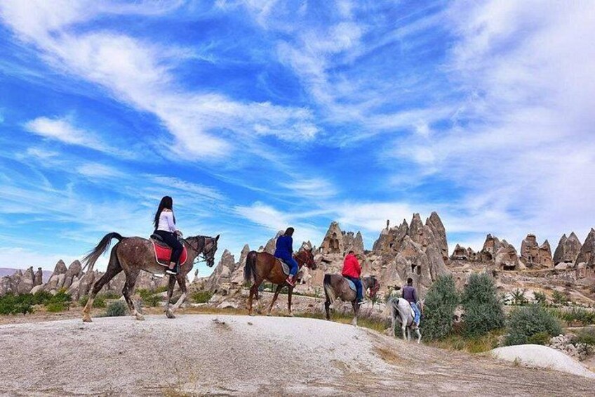 People riding horses on a rocky terrain with unique rock formations in the background. 1
