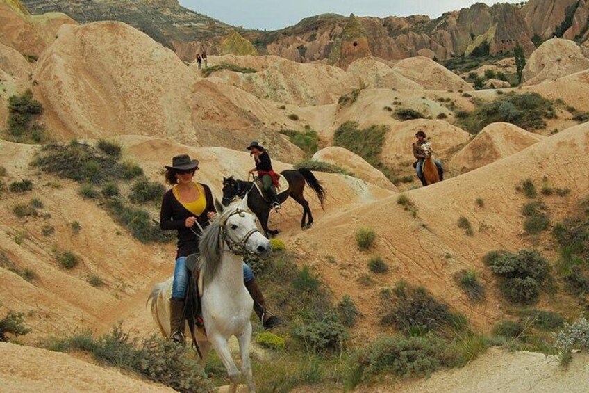 A person riding a white horse on a dirt path through a desert landscape with rolling hills and sparse vegetation. 4