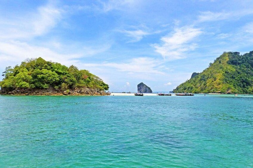 A turquoise sea with a small island covered in green foliage, a large rock formation in the distance, and a clear sky. 5