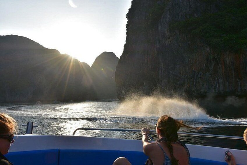 A boat with people enjoying a sunny day, cliffs in the background, and water splashing. 1