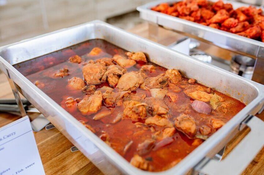 A buffet with a dish of chicken in a red sauce. 3