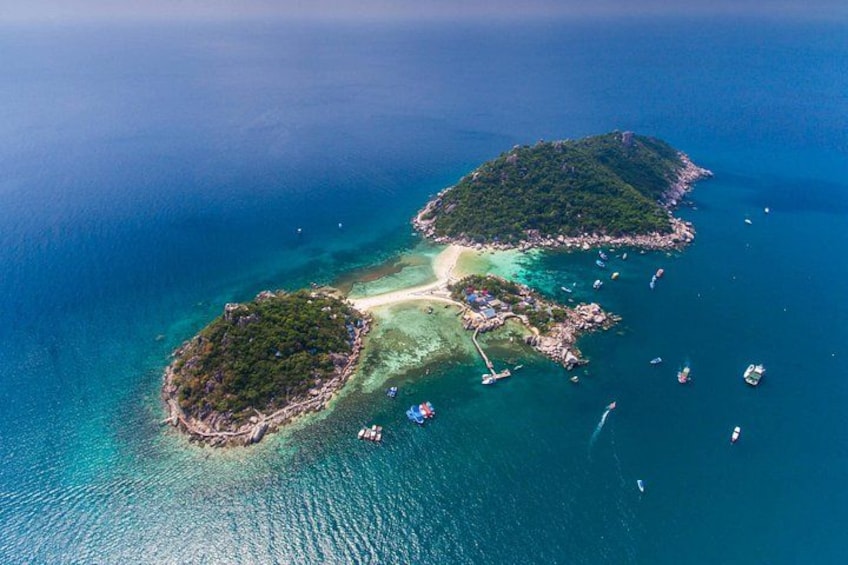 An aerial view of a tropical island with clear turquoise waters, a sandy beach, and a small settlement with boats. 3