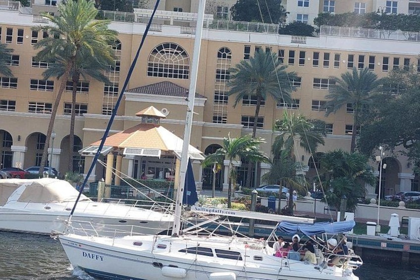 Een witte jacht genaamd 'DAFFY' ligt afgemeerd in een jachthaven, met palmbomen en een gebouw op de achtergrond. 2