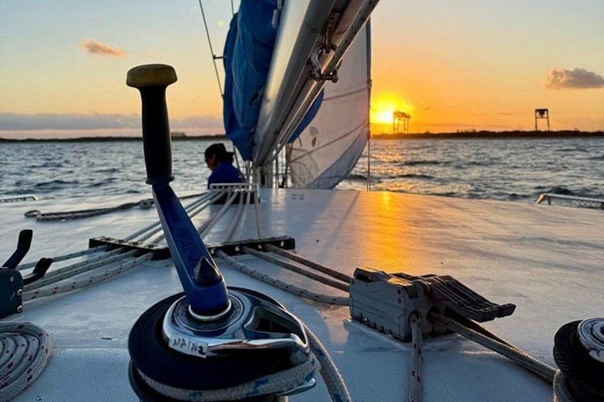 Un voilier au coucher du soleil, avec une personne qui rame, une voile et une côte lointaine. 2