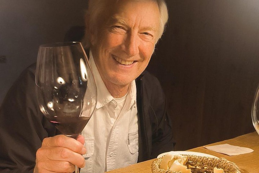 Een persoon houdt een wijnglas vast, zittend aan een tafel met een mandje brood. 1
