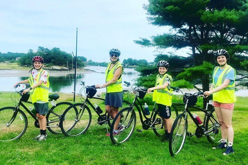 Four people wearing safety vests standing next to bicycles by a lake. 2