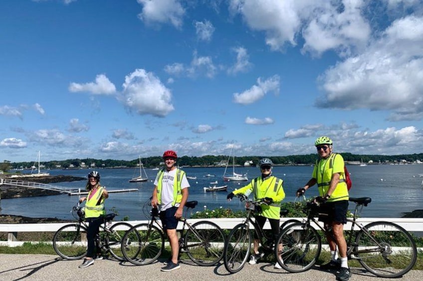 Four people with bicycles near a waterfront with boats and a clear sky. 4