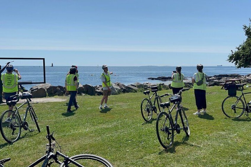 A group of people in safety vests by a coastal area with bicycles. 2