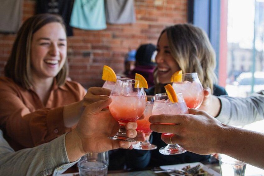People toasting with pink drinks garnished with orange slices. 2