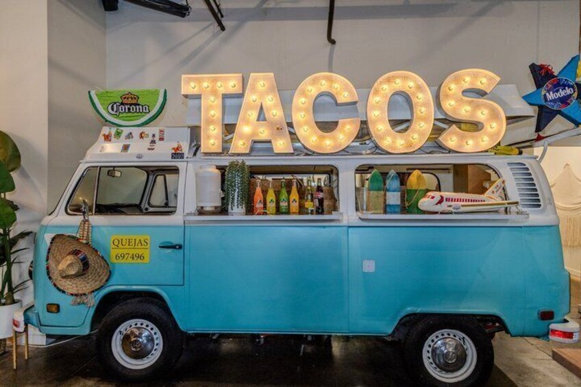 A vintage blue van with a taco stand, Corona beer sign, and a Model T sign. 4