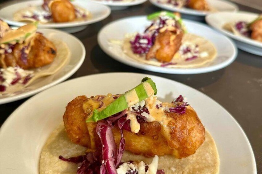 A plate of food with a golden-brown item, possibly a fried fish, on a tortilla, garnished with green onions and purple cabbage, and a creamy sauce. 2