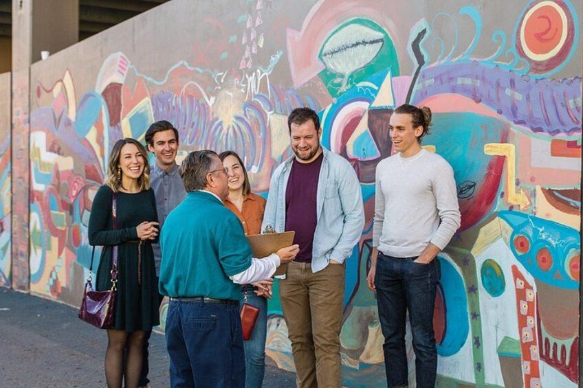 A group of people standing in front of a colorful mural. 4