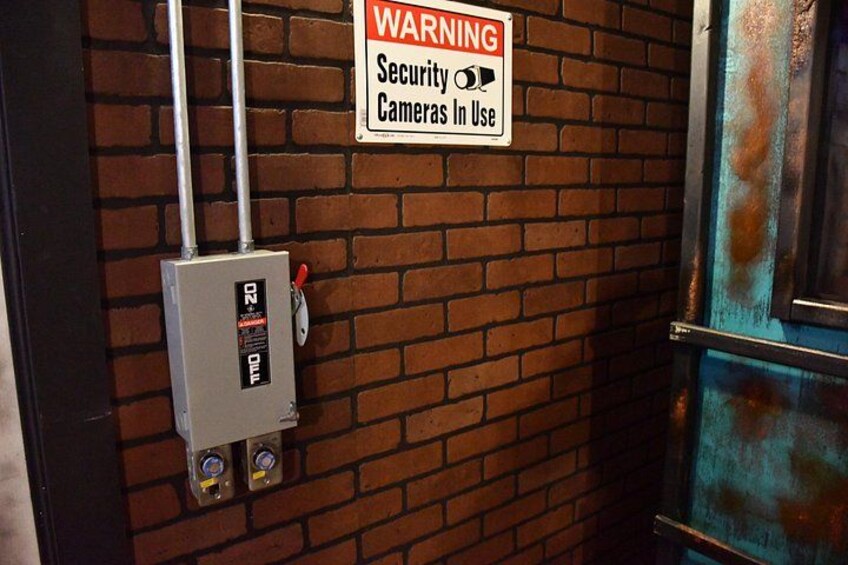 A security warning sign, a metal box with a red button, and a door with a rusty frame. 2