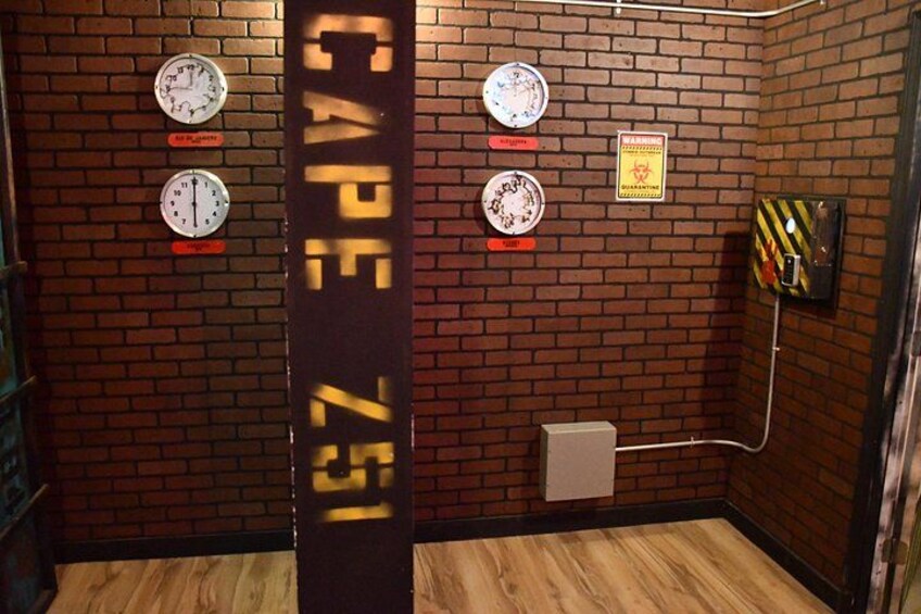 A brick-walled room with four clocks, a fire alarm, and a warning sign. 3