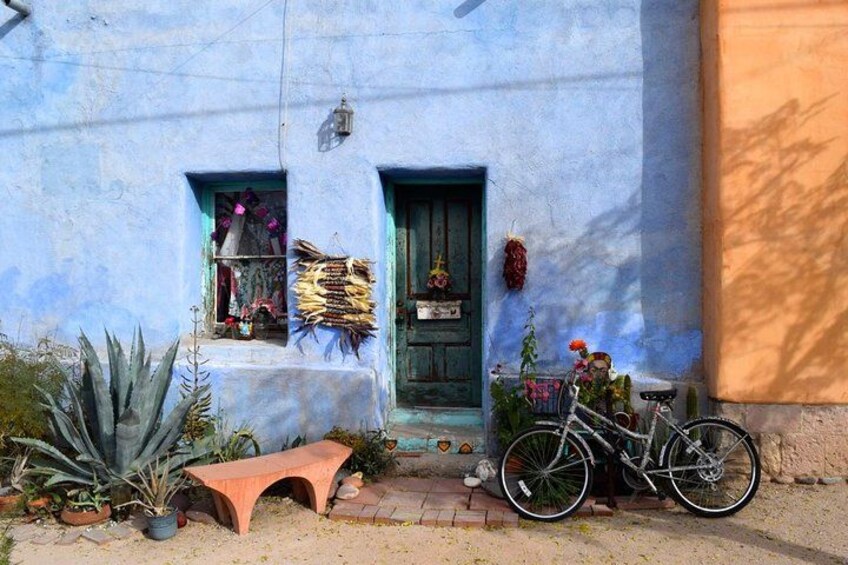 Una casa azul con puerta verde, una bicicleta y varias plantas y adornos. 2