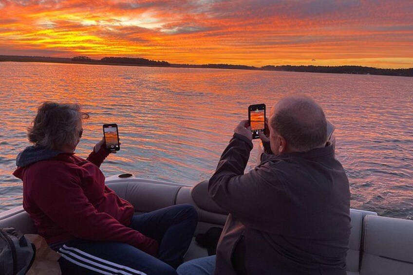 Two people on a boat taking photos of a sunset over water. 2