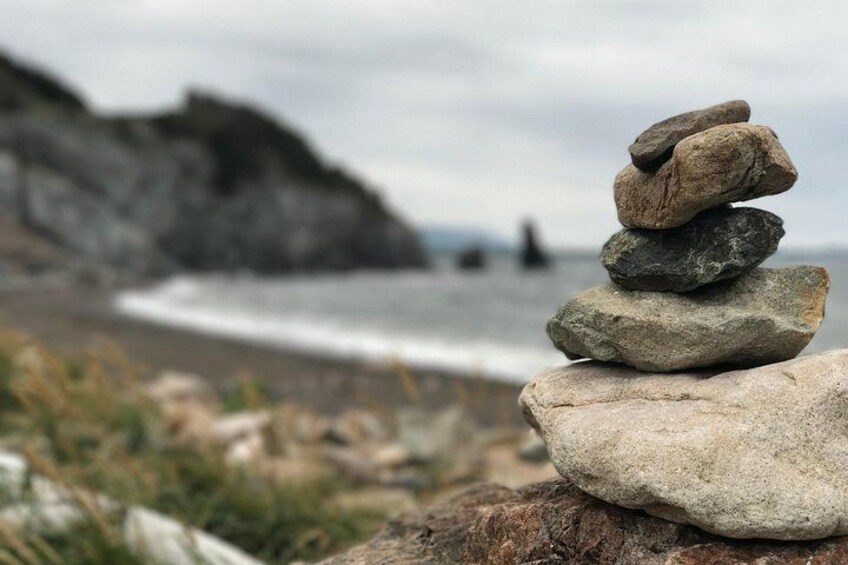 A stack of rocks on a beach with a rocky cliff and ocean in the background. 2