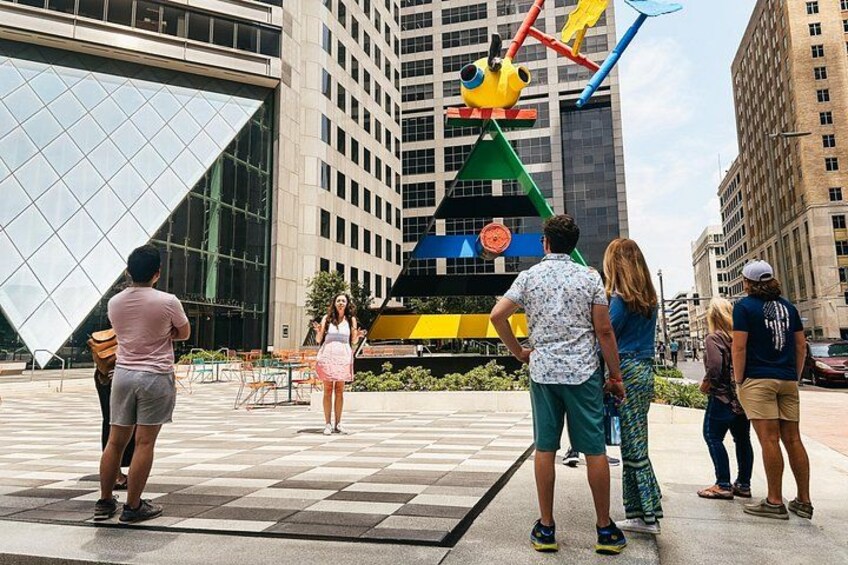 Un grupo de personas de pie en una plaza con un edificio de cristal grande y una escultura colorida al fondo. 5