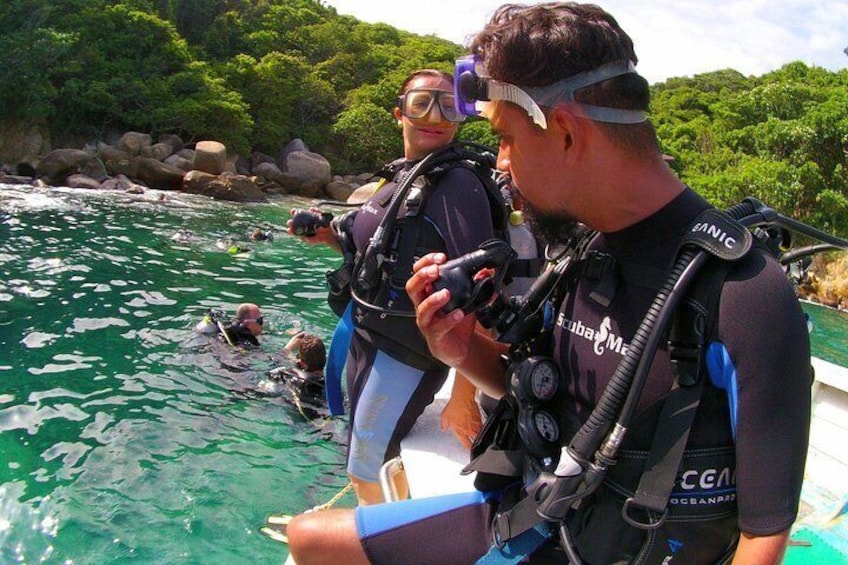 Two people in scuba diving gear on a boat, with a diver in the water. 2