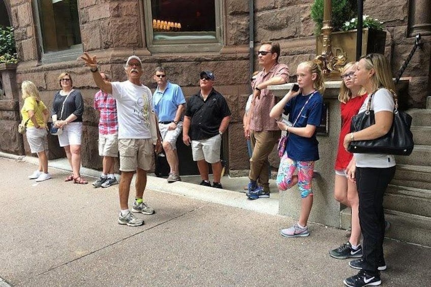 A group of people standing on a sidewalk, some looking at a street performer. 2