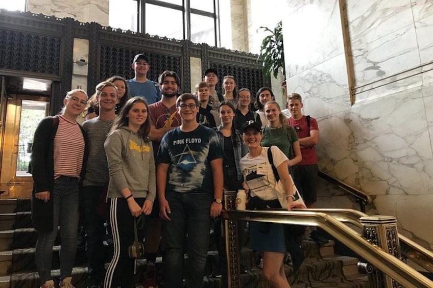 A group of people on a staircase in a building with marble walls and a patterned wall. 3