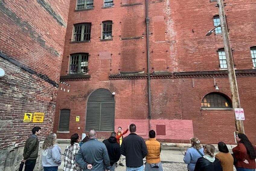 A group of people standing in front of a red brick building with arched windows and a large door. 3