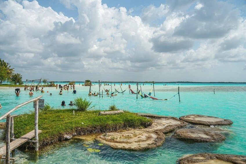 Una playa tropical con agua turquesa cristalina, pasarelas de madera y gente nadando y relajándose. 3