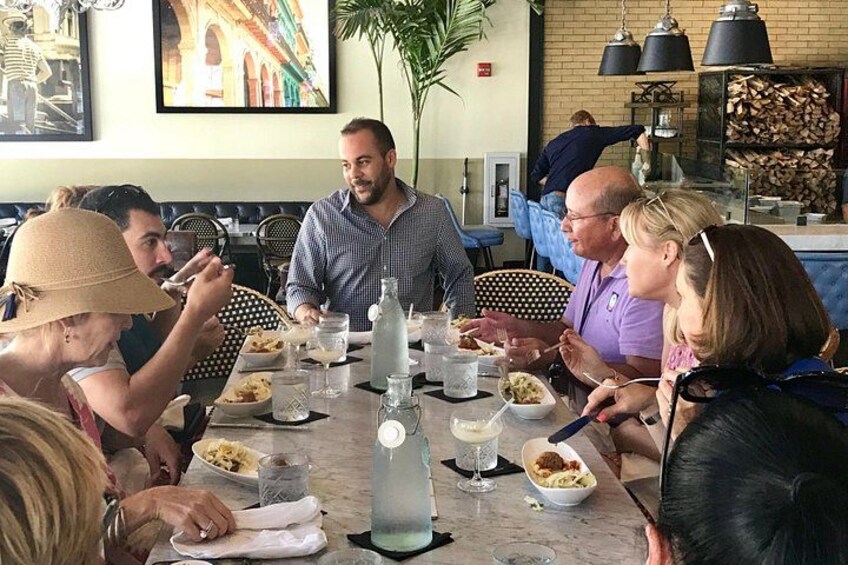 A group of people dining at a restaurant with a large table, chairs, and various dishes. 4