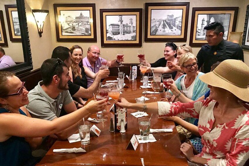 A group of people toasting at a wooden table in a restaurant with framed pictures on the wall. 3