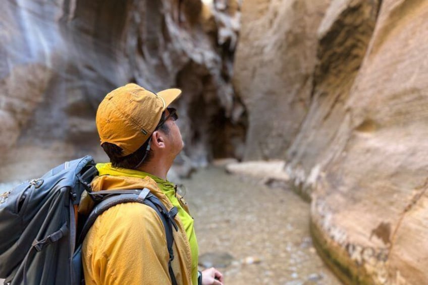 Un escursionista in un canyon, con uno zaino, terreno roccioso e un piccolo corso d'acqua. 1