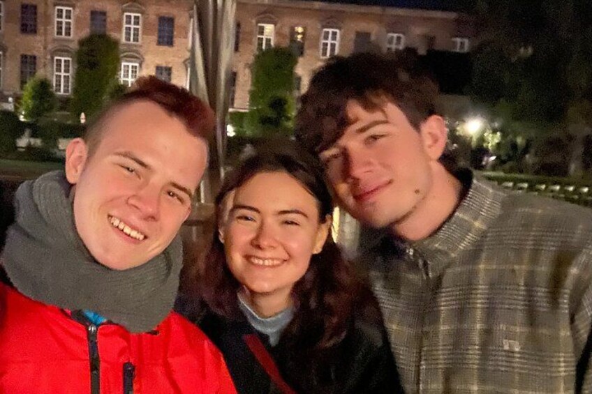 Drie personen buiten 's nachts, met gebouwen op de achtergrond. 3