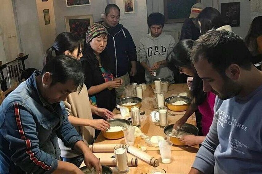 Un grupo de personas participa en una actividad culinaria alrededor de una mesa de madera, con utensilios de cocina e ingredientes. 3