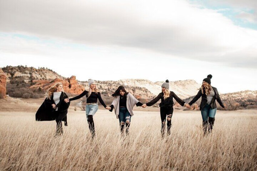 Five people holding hands in a field with red rock formations in the background. 1