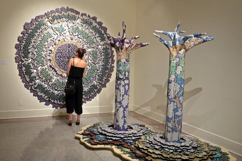 Una persona observa una gran obra de arte circular en la pared, con dos esculturas altas, similares a árboles, en primer plano. 4