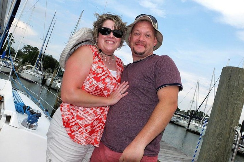A marina with boats, a wooden dock, and a person wearing a hat and a purple shirt. 1