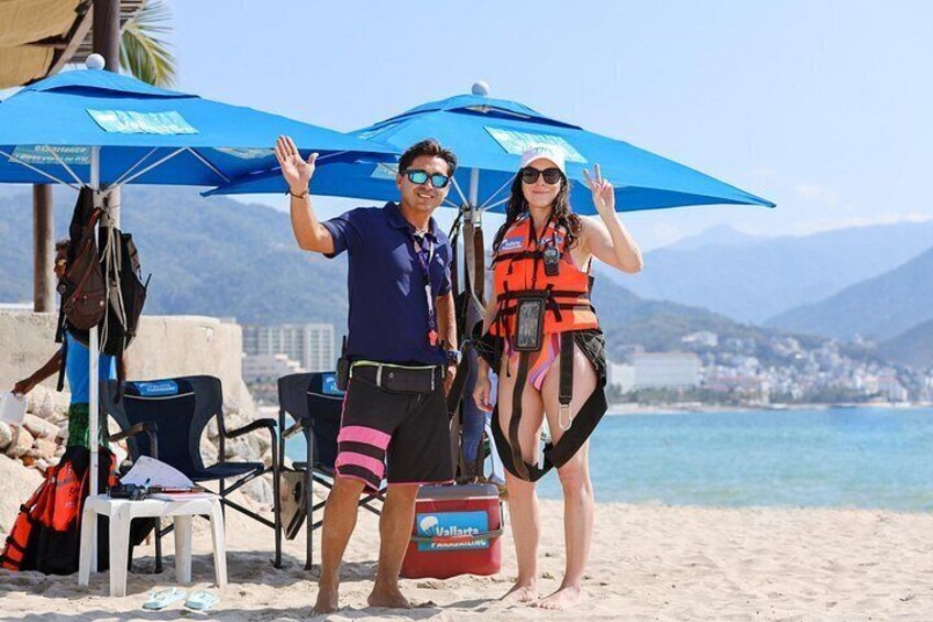 Two people on a beach with a blue umbrella, a red cooler, and a chair. 2
