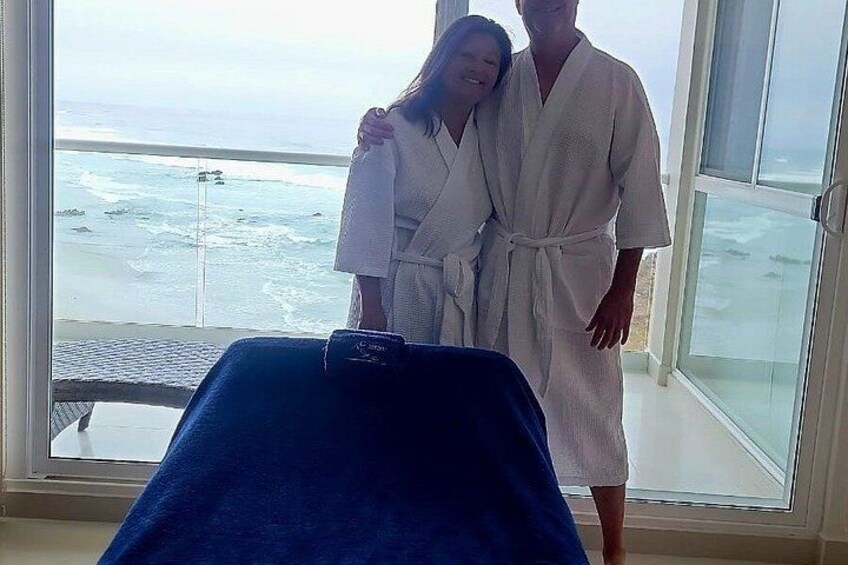 A couple in white robes standing by a massage table with a view of the ocean. 5