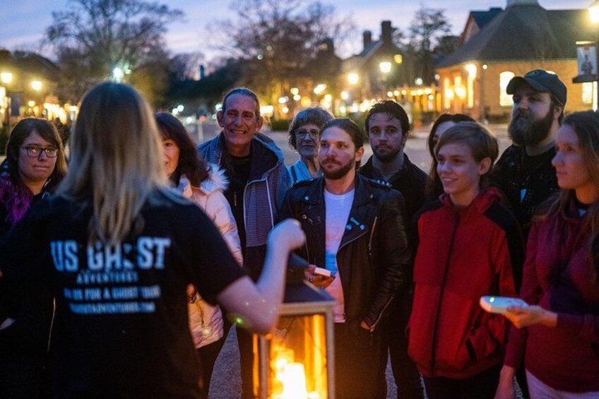 Un grupo de personas reunidas alrededor de una mesa con una vela encendida, en un entorno al aire libre con edificios al fondo. 3