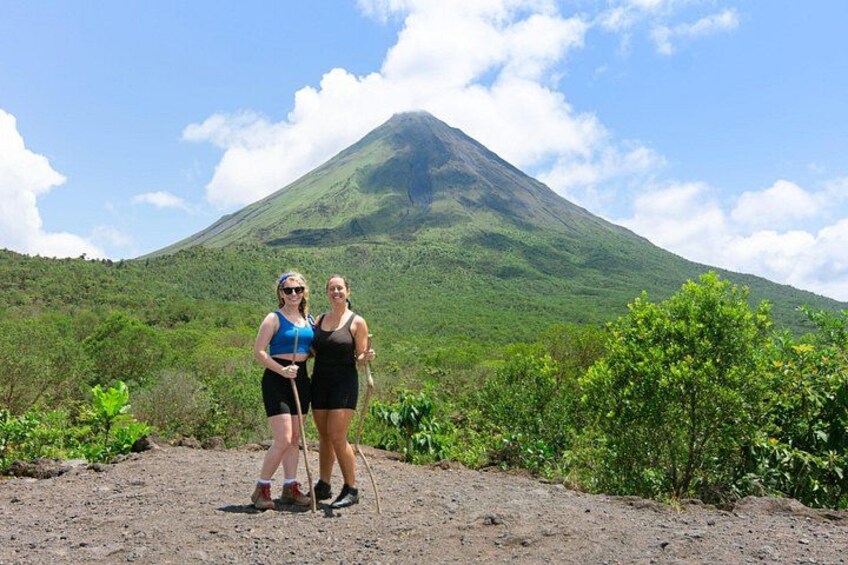 Two people standing in a natural landscape with a volcano in the background. 2