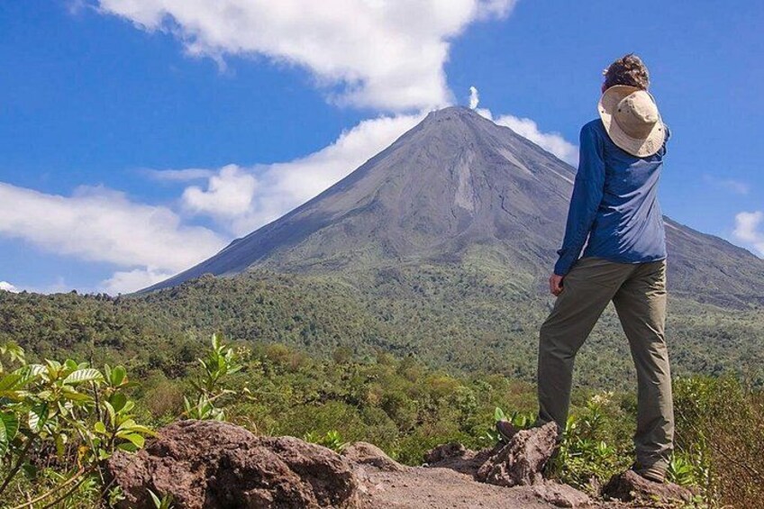 A person standing on a rocky outcrop overlooking a volcano with a clear sky. 3