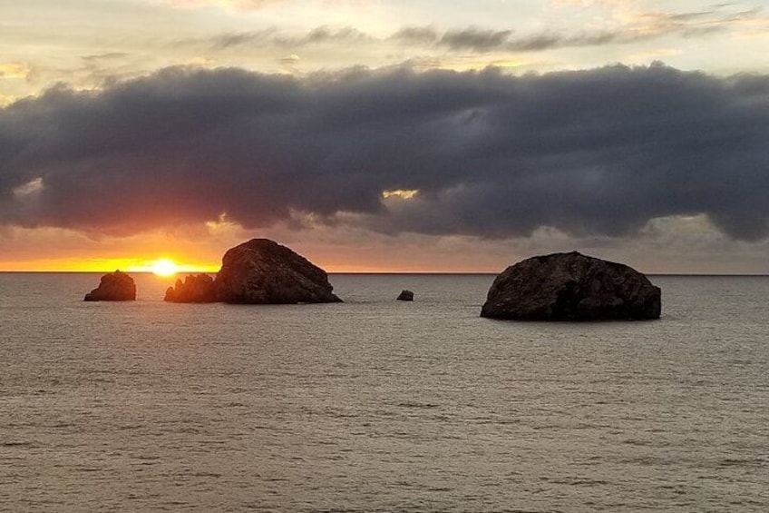 Un atardecer sobre el océano con tres rocas grandes en el agua. 4