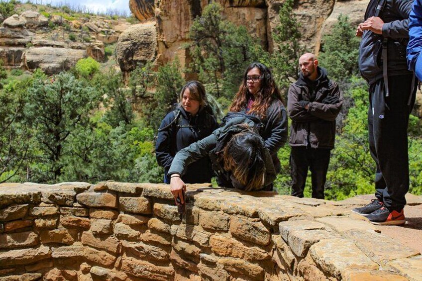 A group of people standing on a stone ledge with a rocky canyon in the background. 3